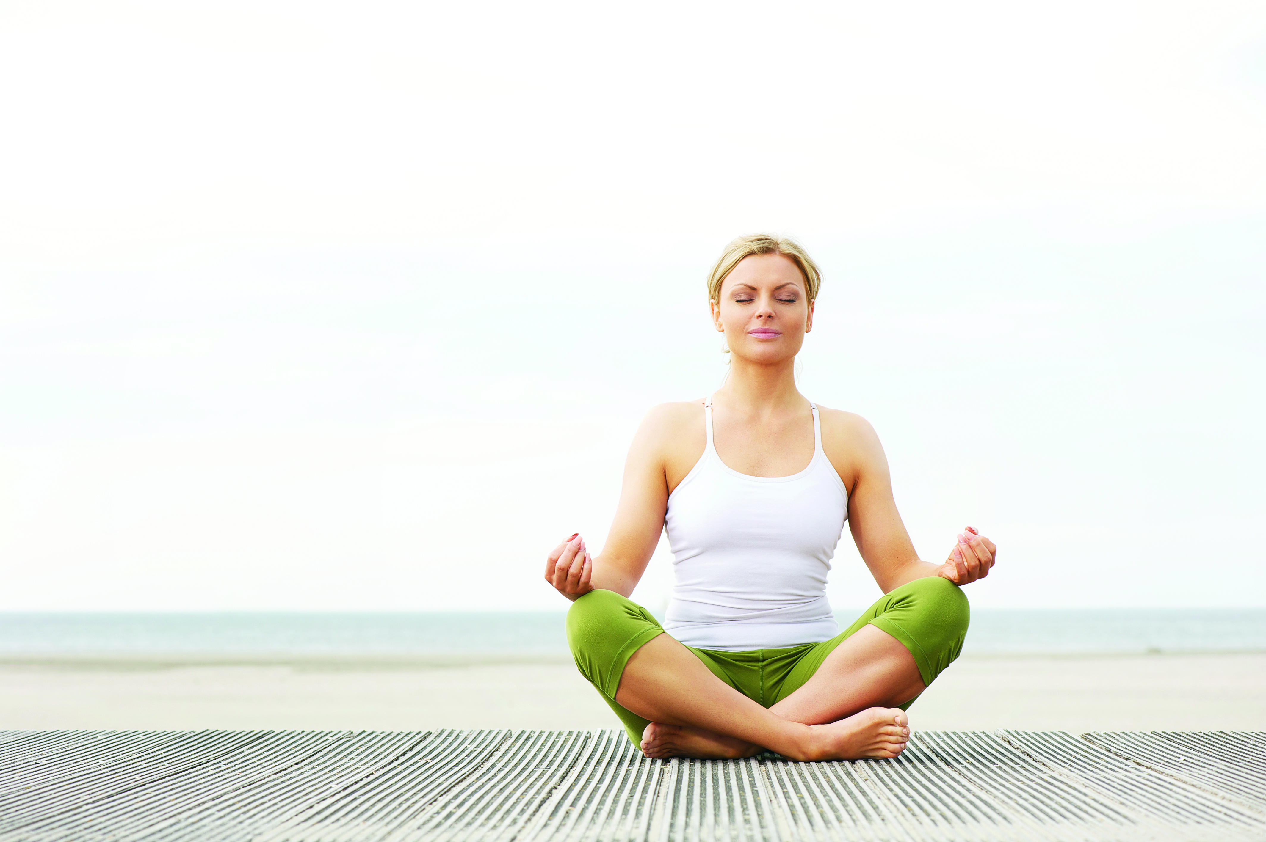 Beautiful young woman sitting in yoga lotus pose at beach